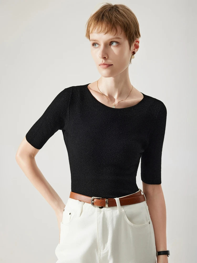 Woman wearing a black top and white pants with a brown belt against a light gray background