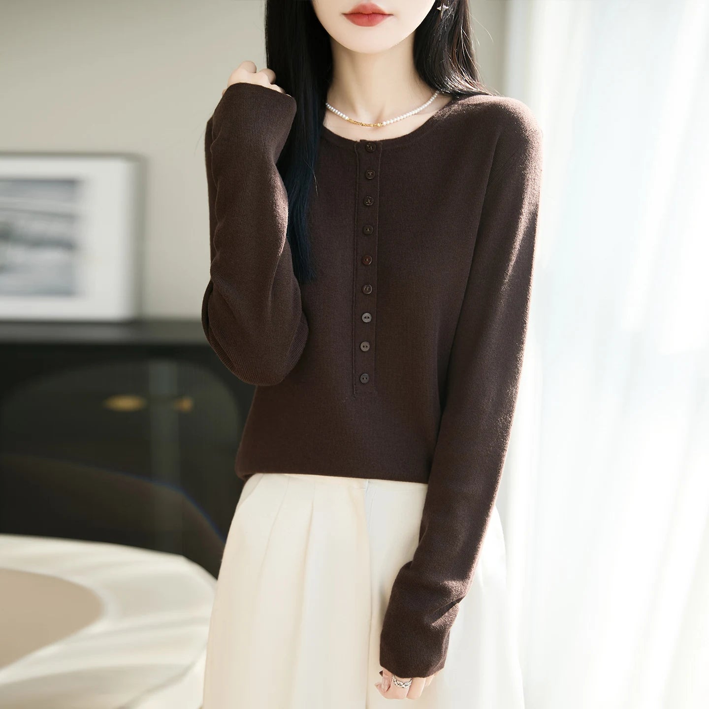 Person wearing a brown long-sleeve shirt with buttons in a neutral indoor setting