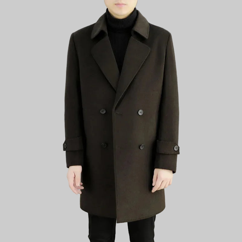 Person wearing a dark brown coat in an indoor setting with a white couch and gray wall.