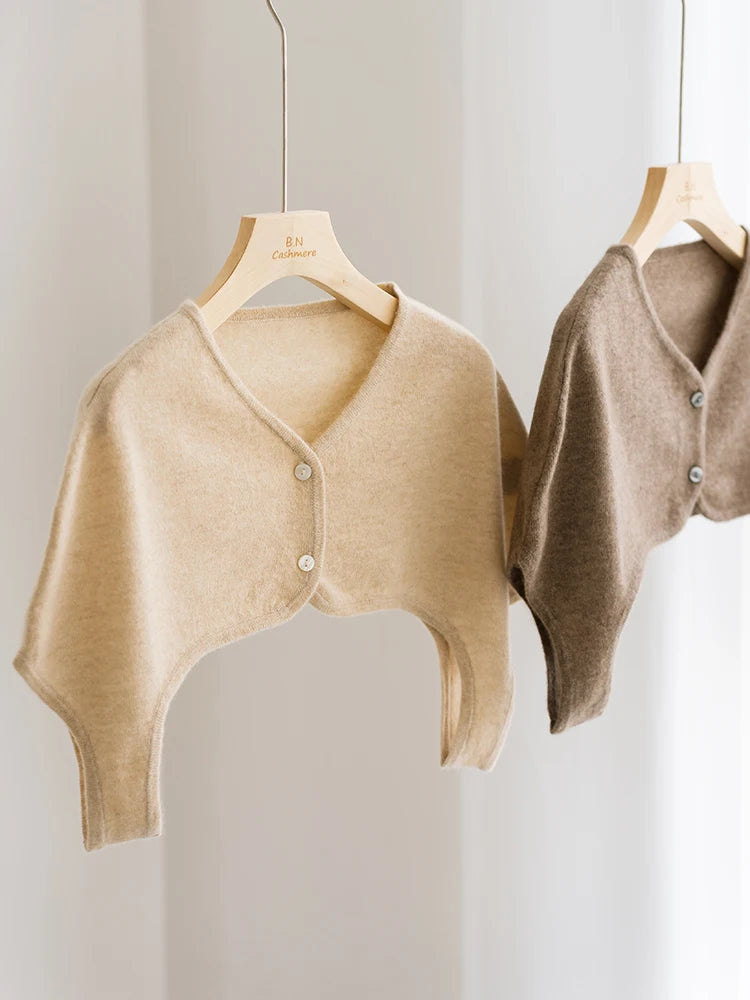 Two beige cardigans hanging on wooden hangers against a light background