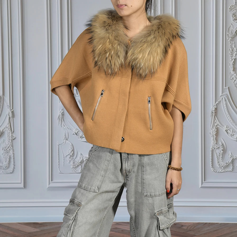 Person wearing a tan jacket with a fur collar against a decorative wall.