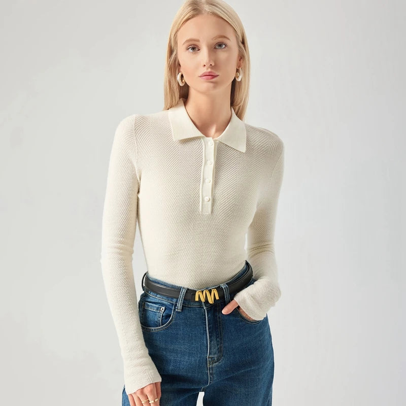 Woman wearing a cream long-sleeve polo shirt and blue jeans on a light gray background