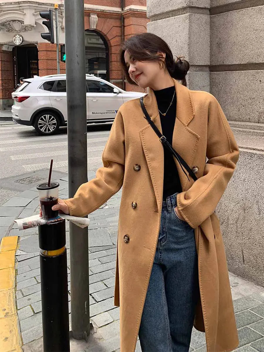 Woman in a tan coat holding a drink on a city street