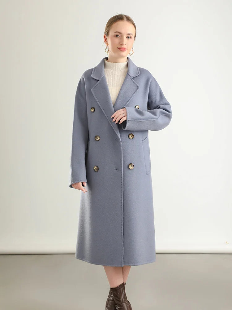 Woman wearing a long gray coat with gold buttons on a plain background