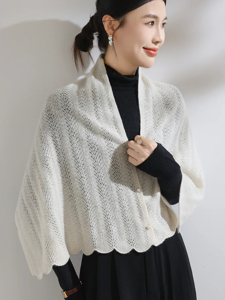 Woman wearing a white knitted shawl over a black outfit against a plain background