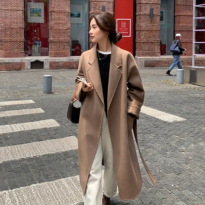 Woman in a long beige coat walking on a city street.