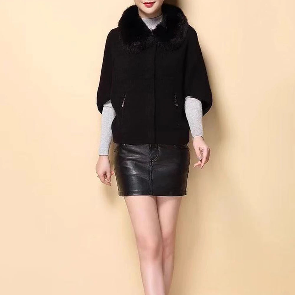 Person wearing a black poncho with fur collar and a black leather skirt on a beige background