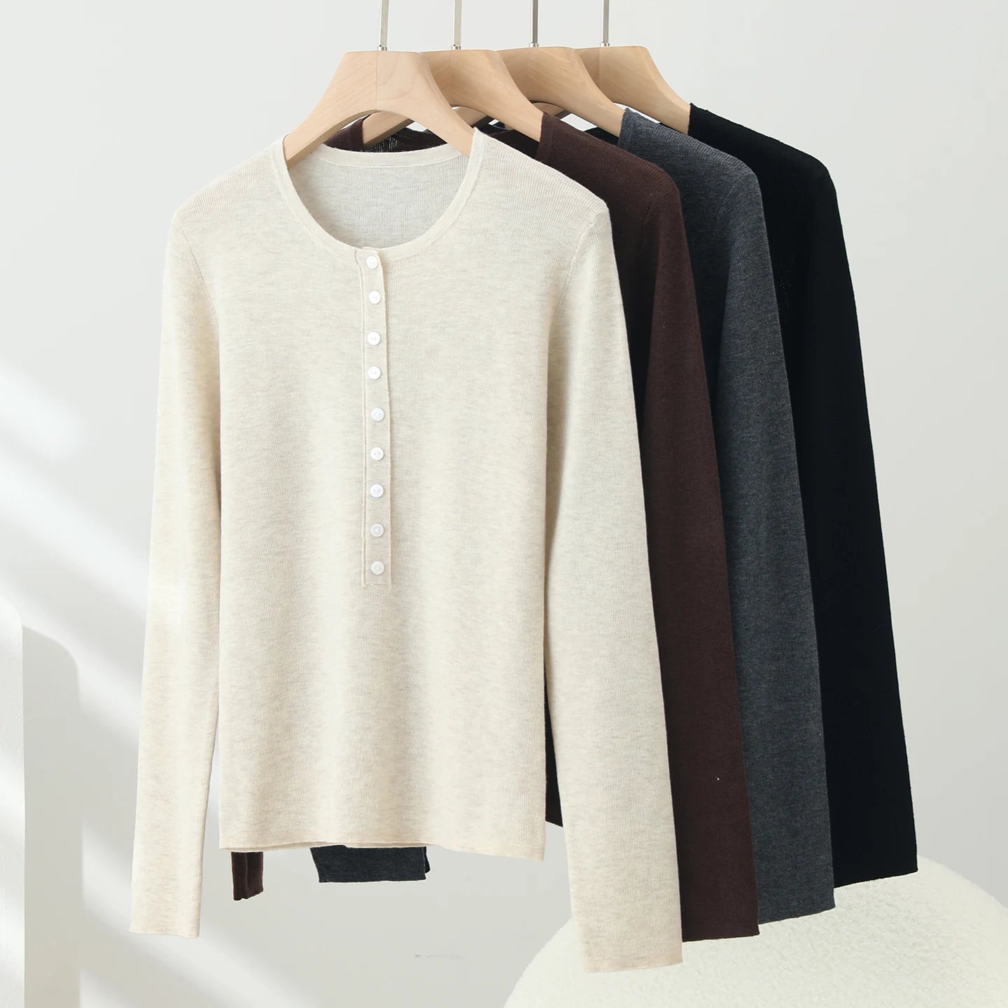 Set of four long-sleeve shirts in beige, brown, gray, and black hanging on a rack against a white background.