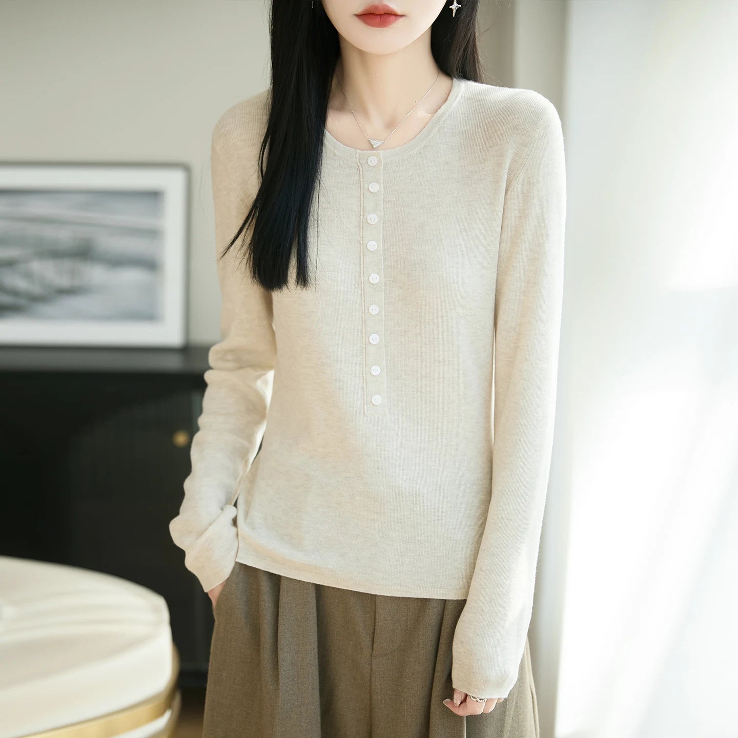 Woman wearing a beige long-sleeve top and brown skirt indoors.