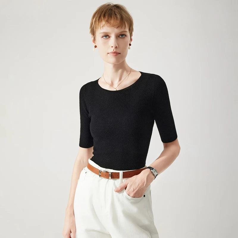 Woman wearing a black top and white pants with a brown belt on a light gray background